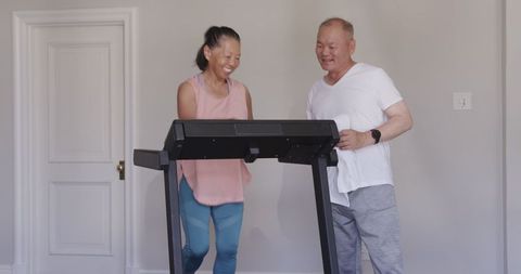 Senior couple laughing while exercising on treadmill at home