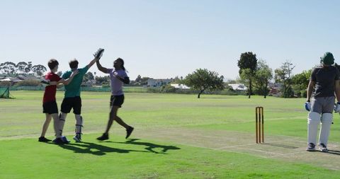 Diverse male cricket players celebrating wicket after keeper dive knocking bails