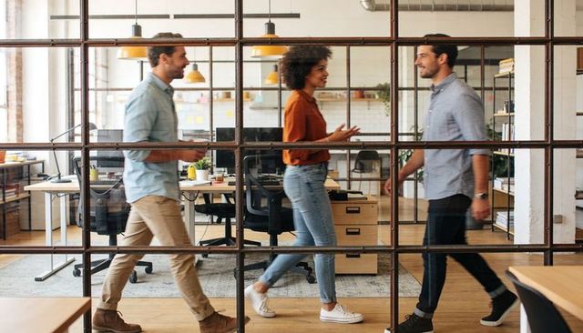 Young coworkers walking and conversing through metal glass grid in modern open-plan office