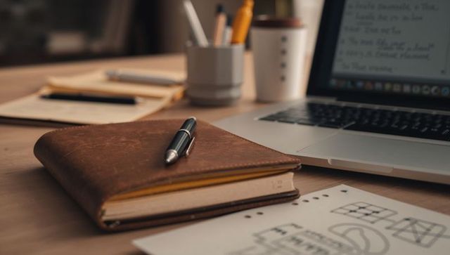 Jotting notes in leather notebook on home office desk with laptop and sketches