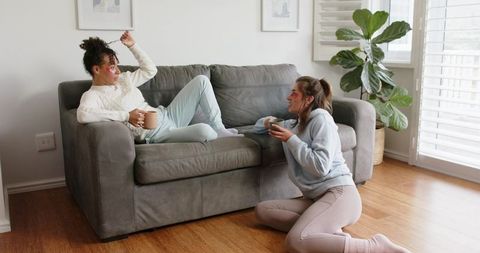 Midlife friends relaxing at home with coffee and under-eye patches on cozy gray couch