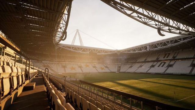 Empty football stadium basking in golden hour light, dramatic shadows across green pitch
