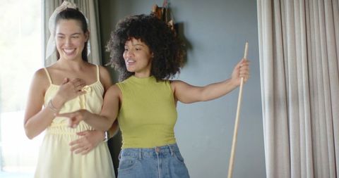 Diverse friends choosing home decor in sunlit living room, laughing and pointing