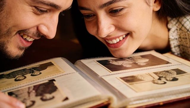 Couple smiling over vintage family album browsing sepia prints, nostalgic memory moment