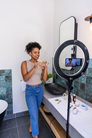 African american influencer demonstrating skincare routine with ring light and smartphone