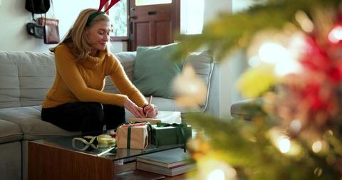 Senior woman writing on gift tags near christmas tree
