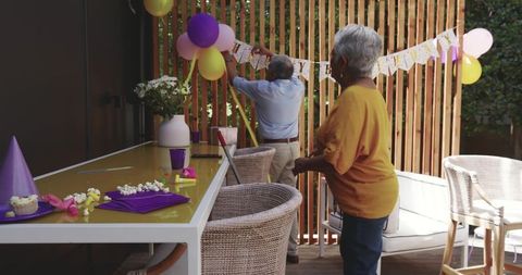 Senior couple decorating backyard deck for birthday celebration with balloons and banner