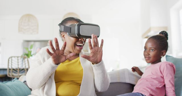 Excited african american grandmother using vr headset sitting with granddaughter at home, copy space. Technology, communication, learning, family and domestic life.