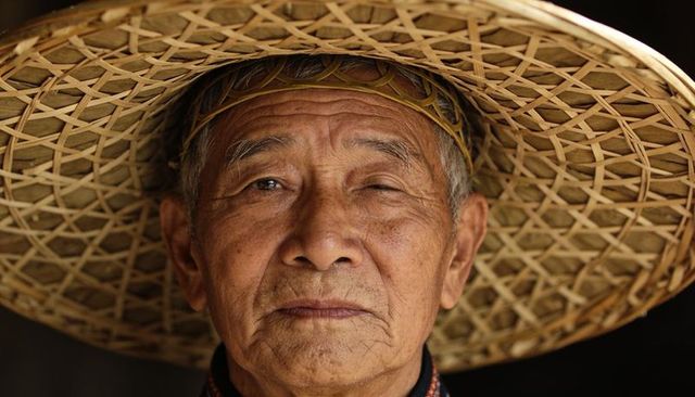 Elderly man wearing wide woven straw hat closeup portrait showing character and culture