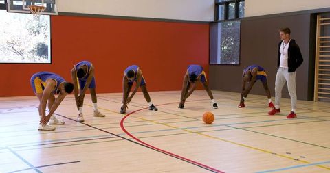 Basketball team warming up with coach on indoor court