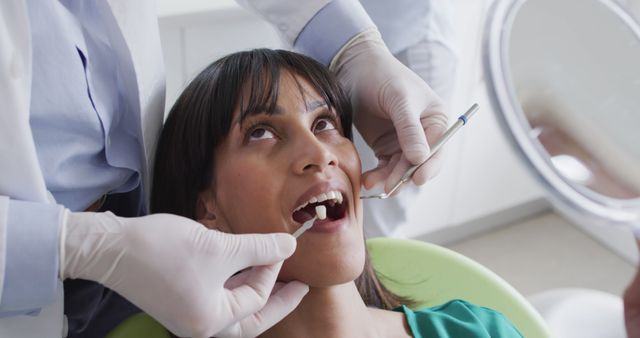 Female patient receiving dental checkup from dentist who is using dental instruments. Ideal for dental care websites, oral health services, medical practices, health insurance brochures, and healthcare pamphlets promoting routine dental exams.