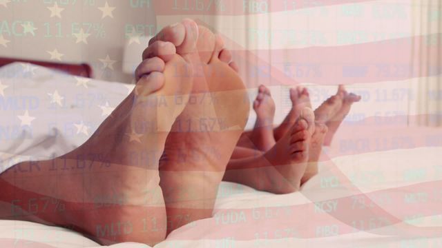 Feet of a Caucasian family lying together in bed, with an overlay featuring the USA flag and financial data. Represents themes of family togetherness, American culture, and financial stability. Useful for articles on family finance, cultural values, and parental relationships in socioeconomic contexts.