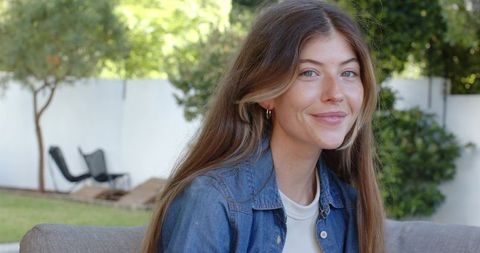 Young woman smiling on outdoor sofa wearing denim jacket and hoop earrings