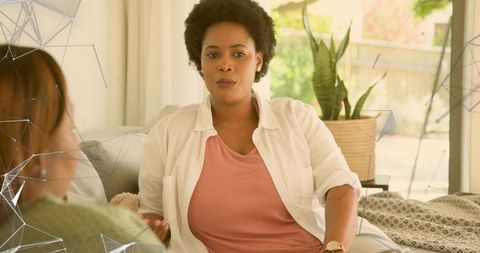 Woman having candid conversation on sofa with friend, cozy living room greenery