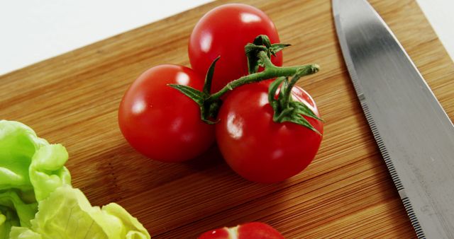 Fresh tomatoes on a wooden cutting board next to a knife and green lettuce. Ideal for content related to healthy eating, cooking tutorials, salad recipes, organic food, or dietary blogs. This is a great visual for promoting culinary knowledge and food preparation tips.
