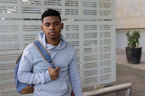 African american teen standing in urban plaza wearing hoodie and backpack, school commute