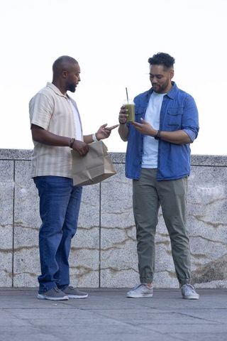 Two african american men pointing at green smoothie while standing on riverside promenade