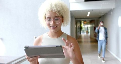 Young professional tapping tablet in bright corridor while colleague sipping coffee