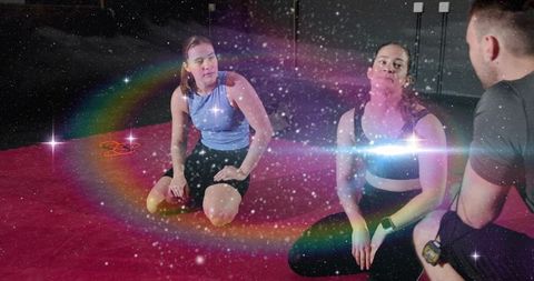Kneeling women pausing during group training with coach on red mat showing resistance bands