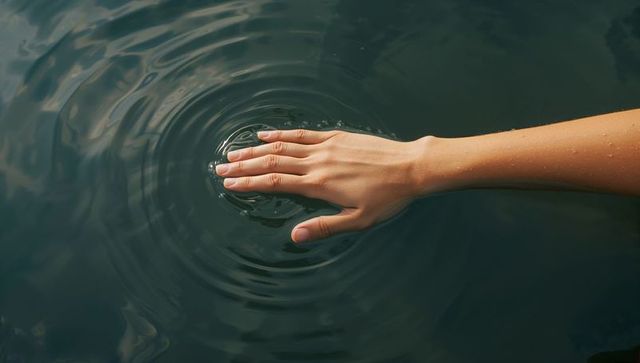 Hand Skimming Calm Lake Surface Creating Concentric Ripples and Water Droplet Sheen