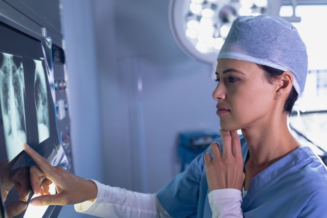 Female surgeon wearing a surgical cap and blue scrubs is studying x-rays on a light box in an operating room. Ideal for concepts related to medical diagnostics, professional healthcare, hospital environments, patient care, and medical expertise.