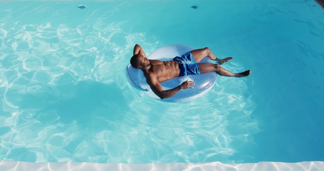 Biracial man having fun sunbathing on inflatable in swimming pool. hanging out and relaxing outdoors in summer.