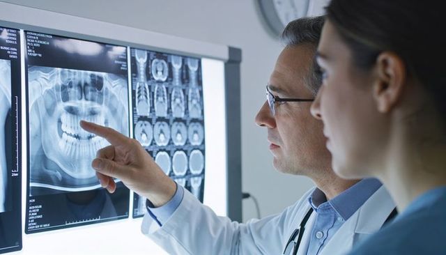 Dentist and trainee reviewing panoramic dental x-ray and ct scans on lightbox