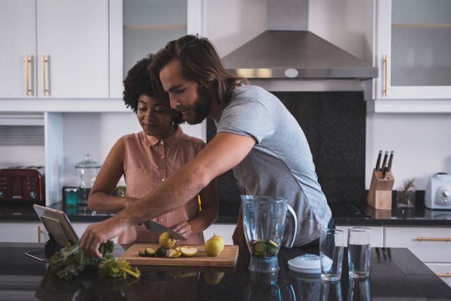 Diverse couple preparing food together in a modern kitchen, using a tablet for recipe guidance. Ideal for content related to home cooking, healthy lifestyle, technology in the kitchen, and relationship bonding. Suitable for articles, blogs, and advertisements focusing on domestic life, quarantine activities, and modern living.