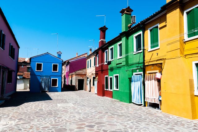 Burano's colorful houses shine under a clear sky, with each home painted vibrantly to reflect Italy's rich culture. These strikingly painted buildings make an excellent backdrop for travel articles, postcards, or content highlighting Mediterranean tourism and European architecture.