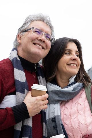 Middle-aged couple smiling and holding coffee cups while wearing scarves on overcast day