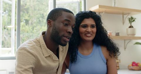 Sunlit diverse couple sharing warm kitchen moment, smiling and leaning close together