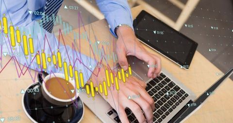 Hands typing on laptop with financial charts overlay, coffee and tablet on wooden desk