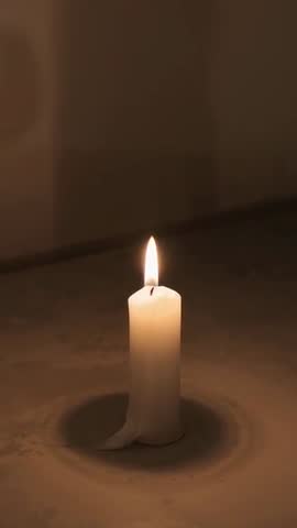 Vertical video burning white pillar candle melting wax on countertop with warm glow