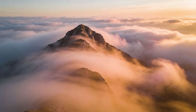 Rising rugged mountain peak emerging through golden clouds at sunrise with sunlit horizon