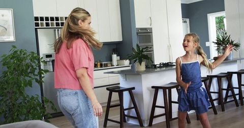 Mother and preteen daughter dancing and singing at kitchen island in modern sunlit home