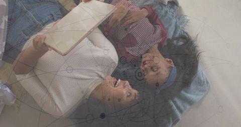 Woman and Girl Sharing Tablet on Blanket with Digital Network Overlay for Family Tech