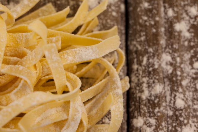 Freshly made fettuccine pasta dusted with flour on a rustic wooden table. Ideal for use in food blogs, Italian cuisine recipes, cooking tutorials, and restaurant menus.