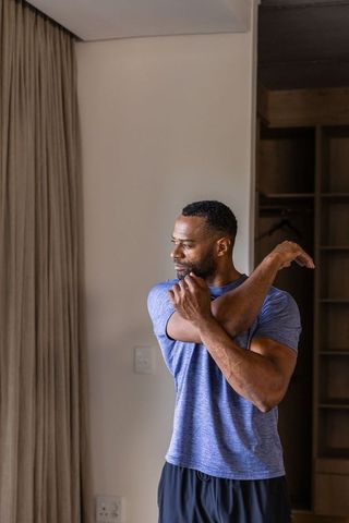 African american man stretching shoulder in minimalist bedroom with natural light