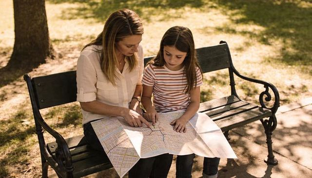 Mother and daughter studying city map on park bench planning weekend route