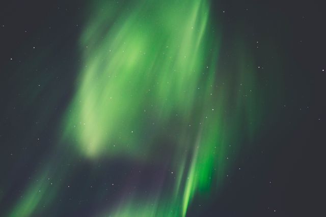 Colorful display of the Northern Lights or Aurora Borealis illuminating the night sky with vivid green hues and scattered stars. Ideal for use in travel brochures, astronomy publications, nature documentaries, screensavers, and wallpapers to depict natural beauty and celestial wonders.