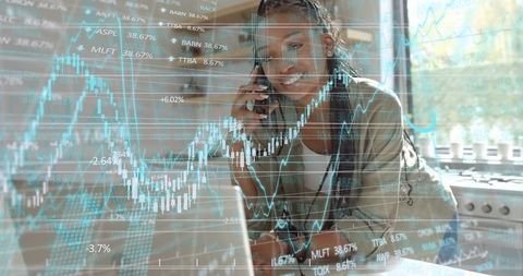 Leaning over laptop making stock trades while talking on phone in bright kitchen
