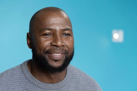 Smiling african american man in gray sweater against turquoise backdrop, bearded headshot