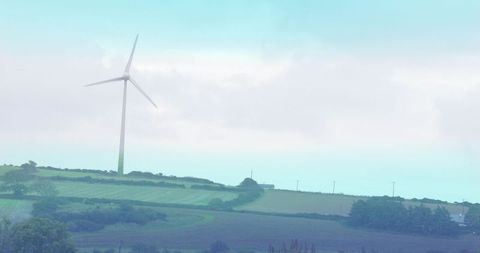 Wind turbine generating clean energy over rolling farmland with hedgerows and utility poles