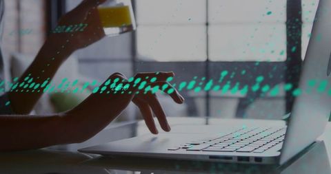 Typing on laptop with teal data overlay and glass of juice in home office