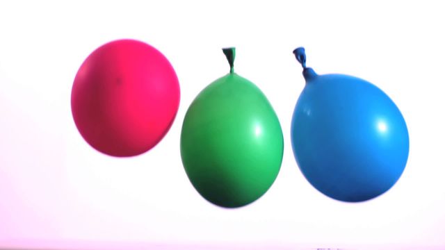 Vibrant colored water balloons float and bounce against a minimal white background, demonstrating playful movement captured in slow motion. Ideal for illustrating fun, festive themes, party invitations, or dynamic energy concepts in advertising and social media posts.