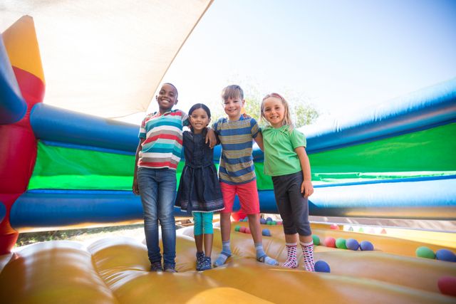 Portrait of friends with arms around standing on bouncy castle at playground