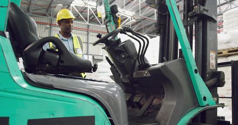 Warehouse Forklift Operator in Yellow Hard Hat and Hi-Vis Vest Inspecting Teal Forklift