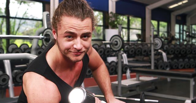Young man lifting a dumbbell in a modern gym with various equipment in the background. Ideal for use in fitness blogs, gym promotional materials, workout guides, or healthy lifestyle campaigns.