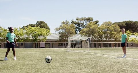Multiracial teenage girls practicing soccer passing on school turf with small goal