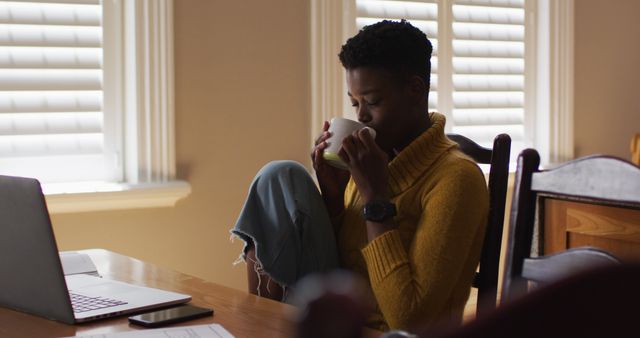 Young woman sipping coffee while working on laptop at home - Download Free Stock Images Pikwizard.com